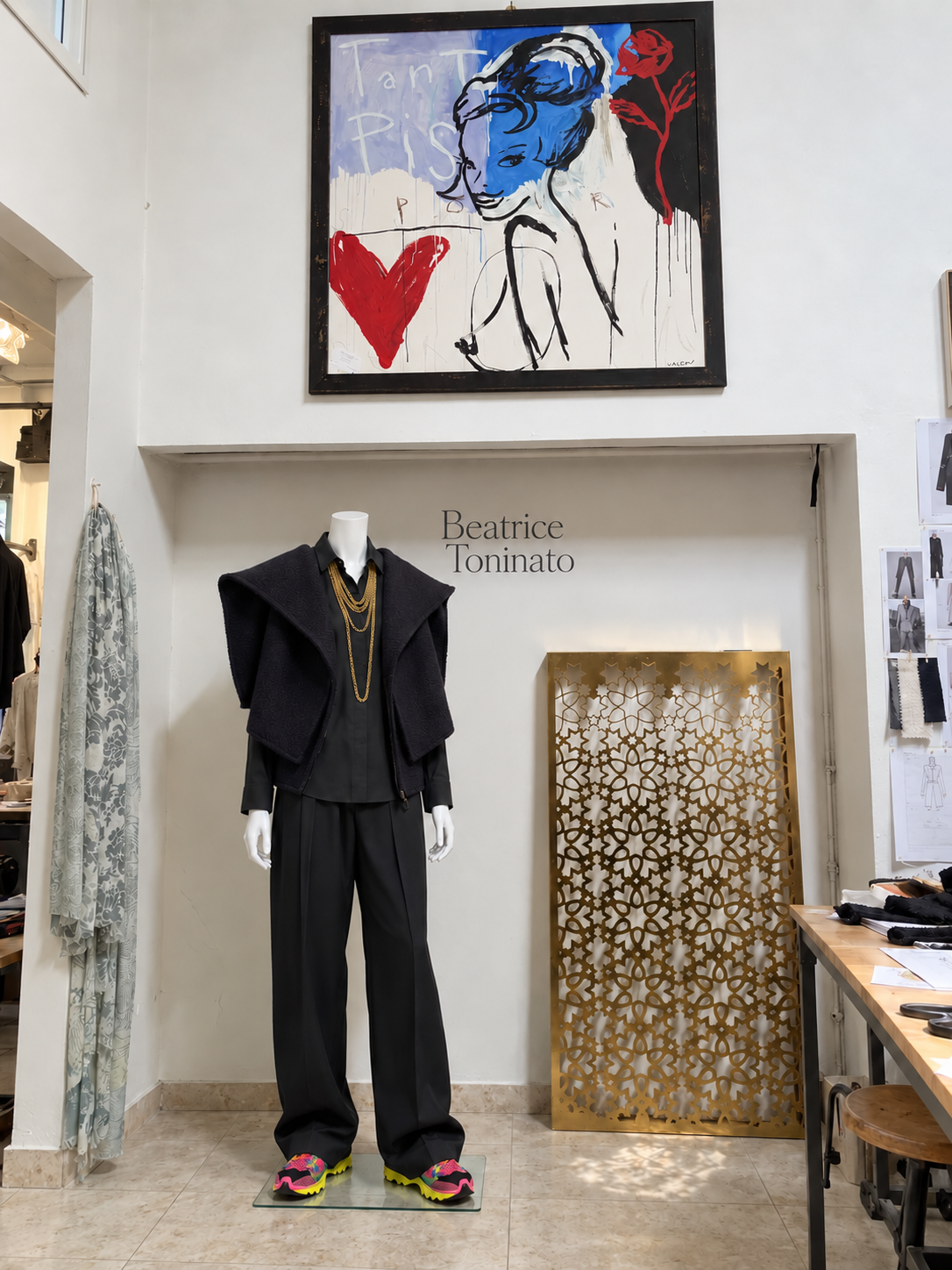 The finished black look on a mannequin: a sleeveless boiled wool jacket with wide folded panels, a black shirt and wide trousers, in front of the Beatrice Toninato logo.