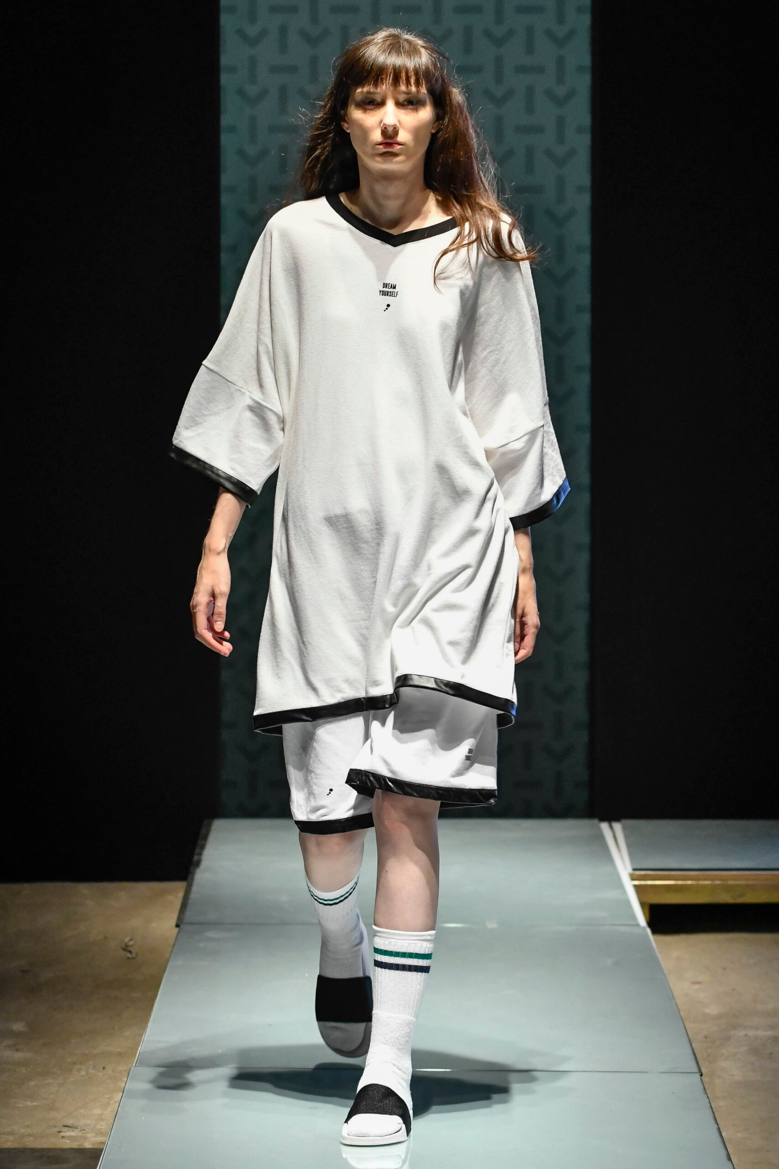 Model on a catwalk in an oversized white T-shirt dress with black trim