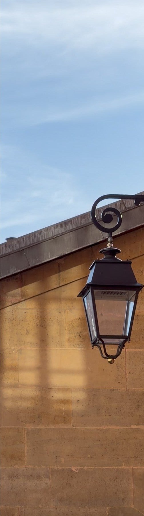 A Paris street lantern against warm stone, a red-brick building and geraniums on a window ledge in Le Marais.