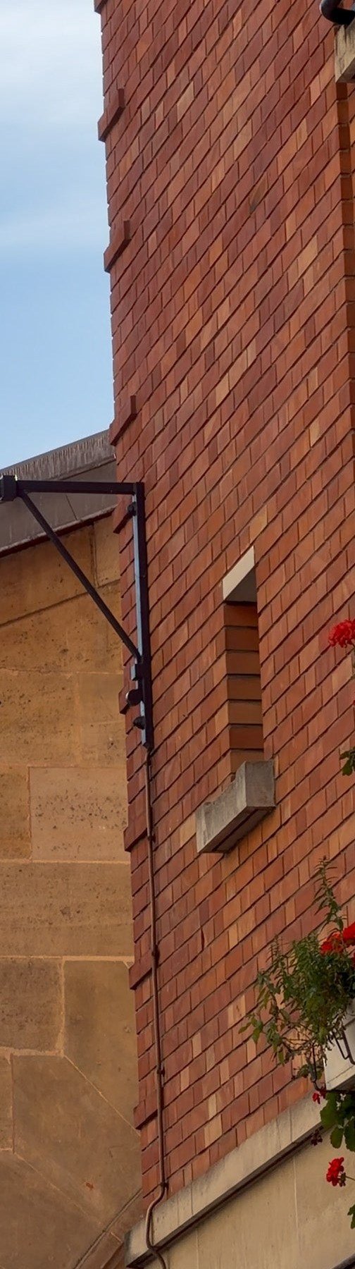 A Paris street lantern against warm stone, a red-brick building and geraniums on a window ledge in Le Marais.